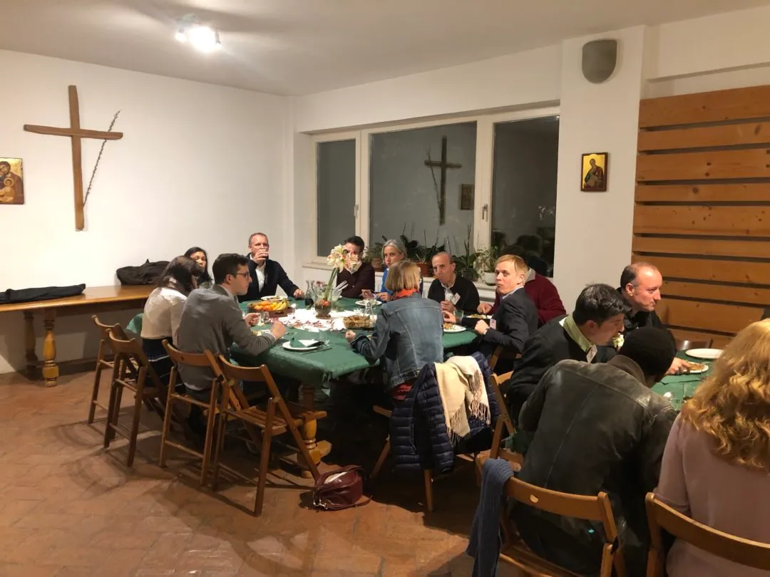 Masă lungă într-o sală parohială, cu adulți și tineri în jurul ei.