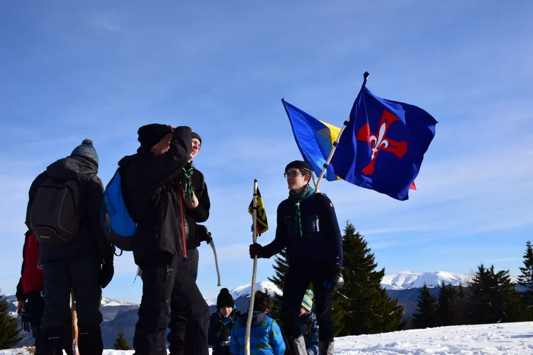 Grup de tineri pe creastă, cu drapelele fluturând, deasupra văilor.