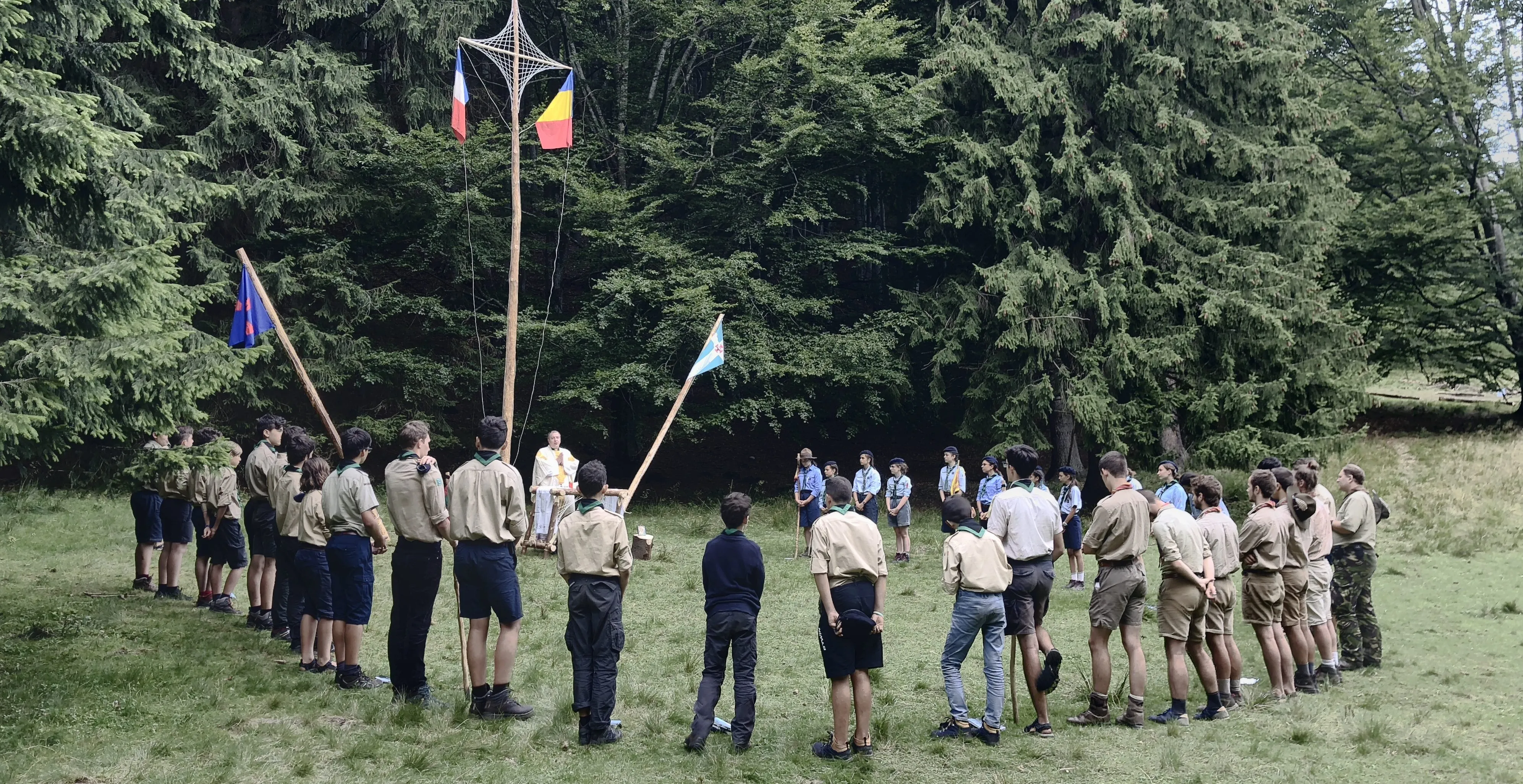 Cercetași adunați în careu într-o poiană de munte.